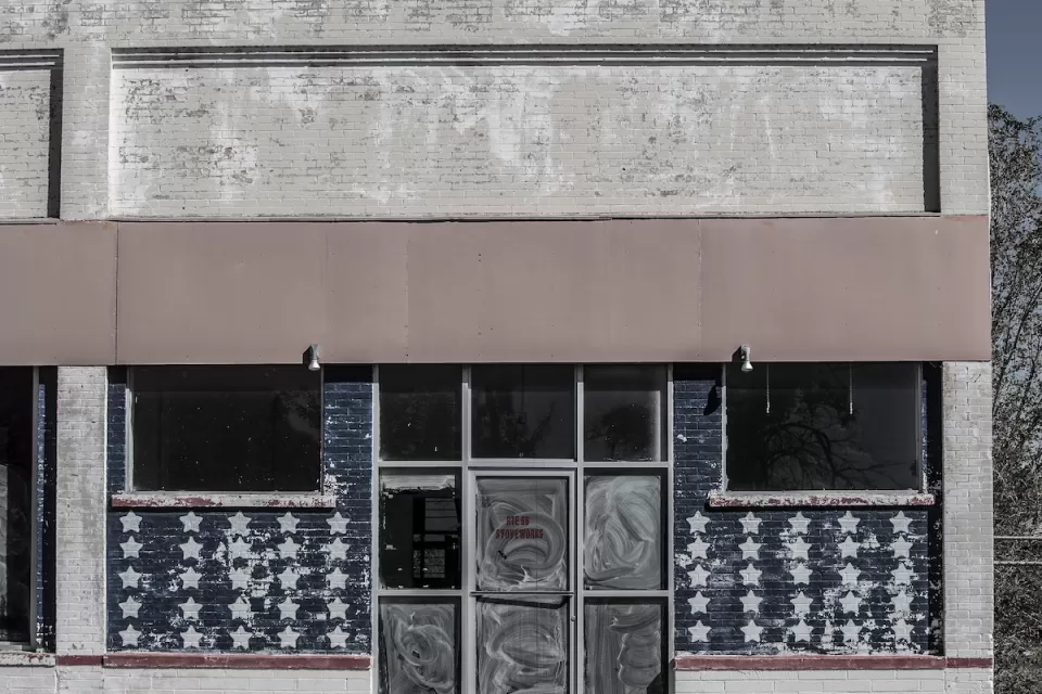 Faded image of vacant storefront in rural area with American flag stars painteind on windows.